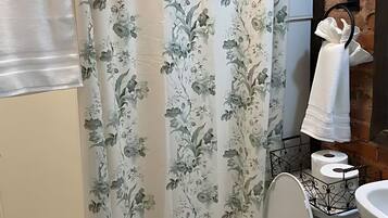 Un baño con inodoro, cortina de ducha con motivos florales, toallero y pared de ladrillo.