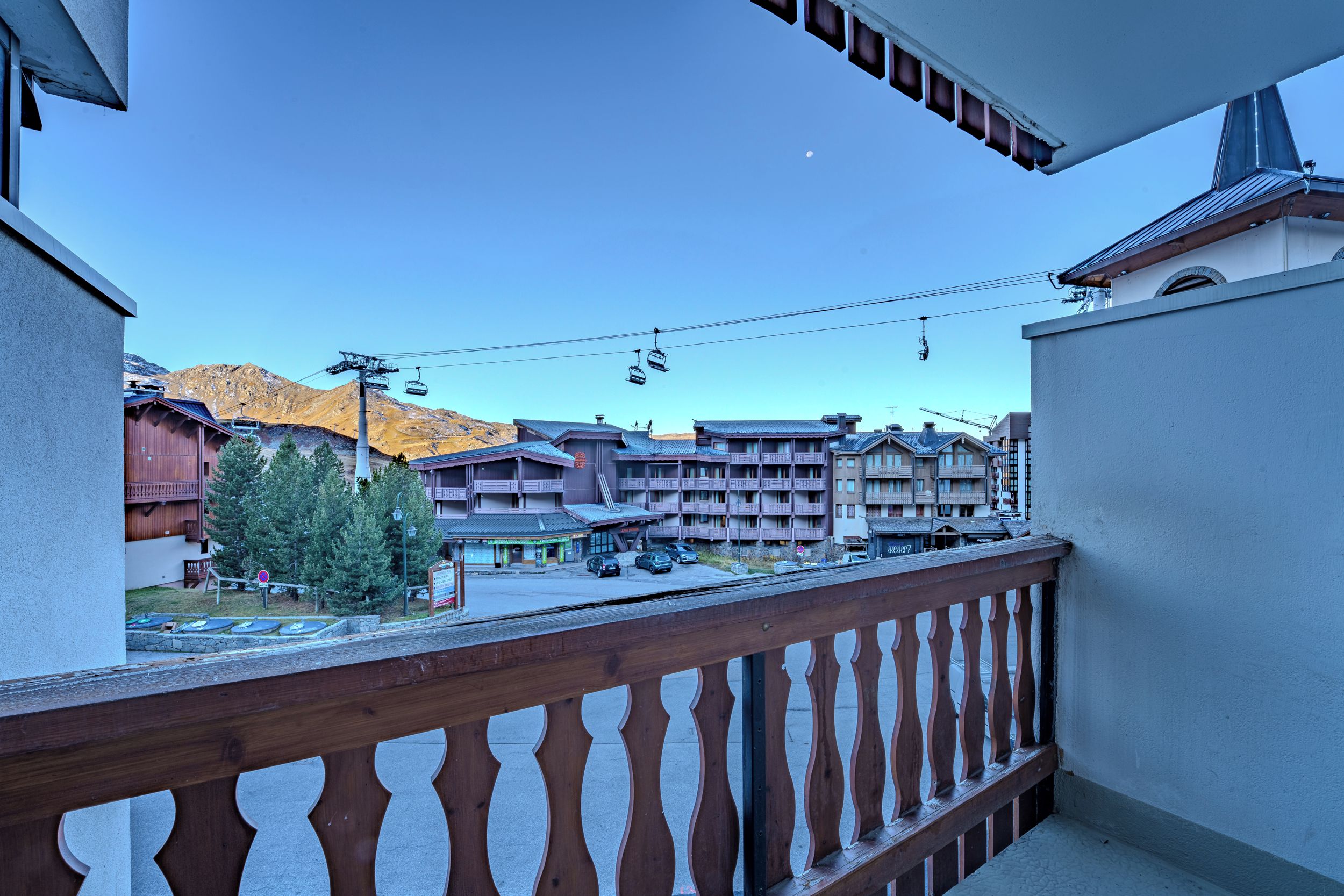 Un balcón con vistas a una montaña, un telesilla y un edificio de varios pisos.