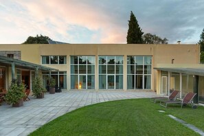 A modern building with large windows, a covered patio area with outdoor seating, and a well-maintained lawn. - QUINTA DAS GERAIS (Marco de Canaveses)