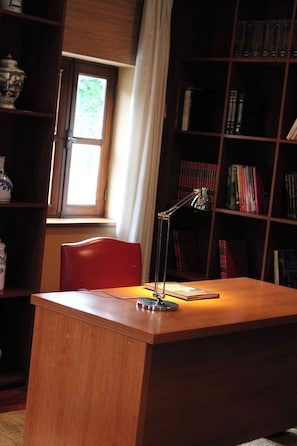 A wooden desk with a lamp, a red chair, and a bookshelf filled with books. - QUINTA DAS GERAIS (Marco de Canaveses)