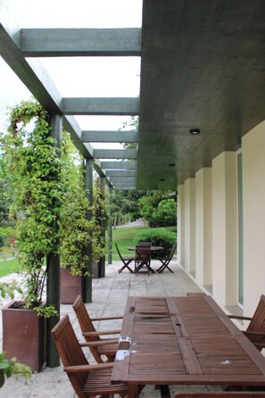 A covered patio area with a table and chairs, surrounded by potted plants and a view of a lawn. - QUINTA DAS GERAIS (Marco de Canaveses)