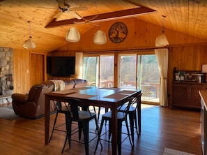 A cozy cabin interior with a dining table, chairs, a sofa, and a television. - Remote River Retreat, Kayak, Fish, Canoe & More (Augusta)