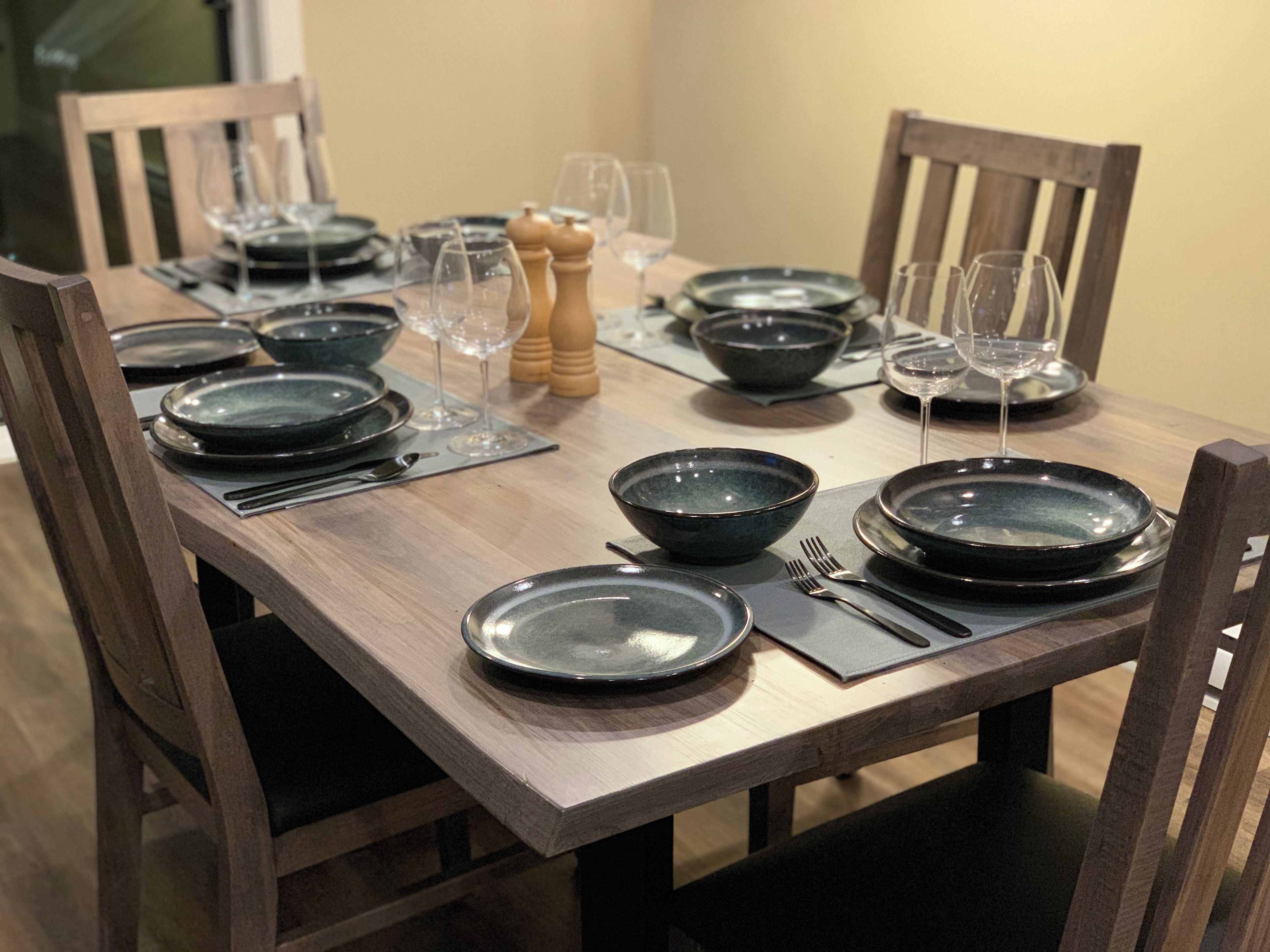 Une table à manger dressée avec des assiettes, des bols, des couverts et des verres, entourée de chaises.