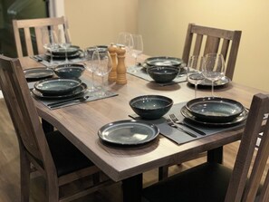 Une table à manger dressée avec des assiettes, des bols, des couverts et des verres, entourée de chaises.