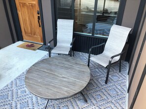 Une table ronde avec deux chaises, une porte en bois et une fenêtre avec des stores.