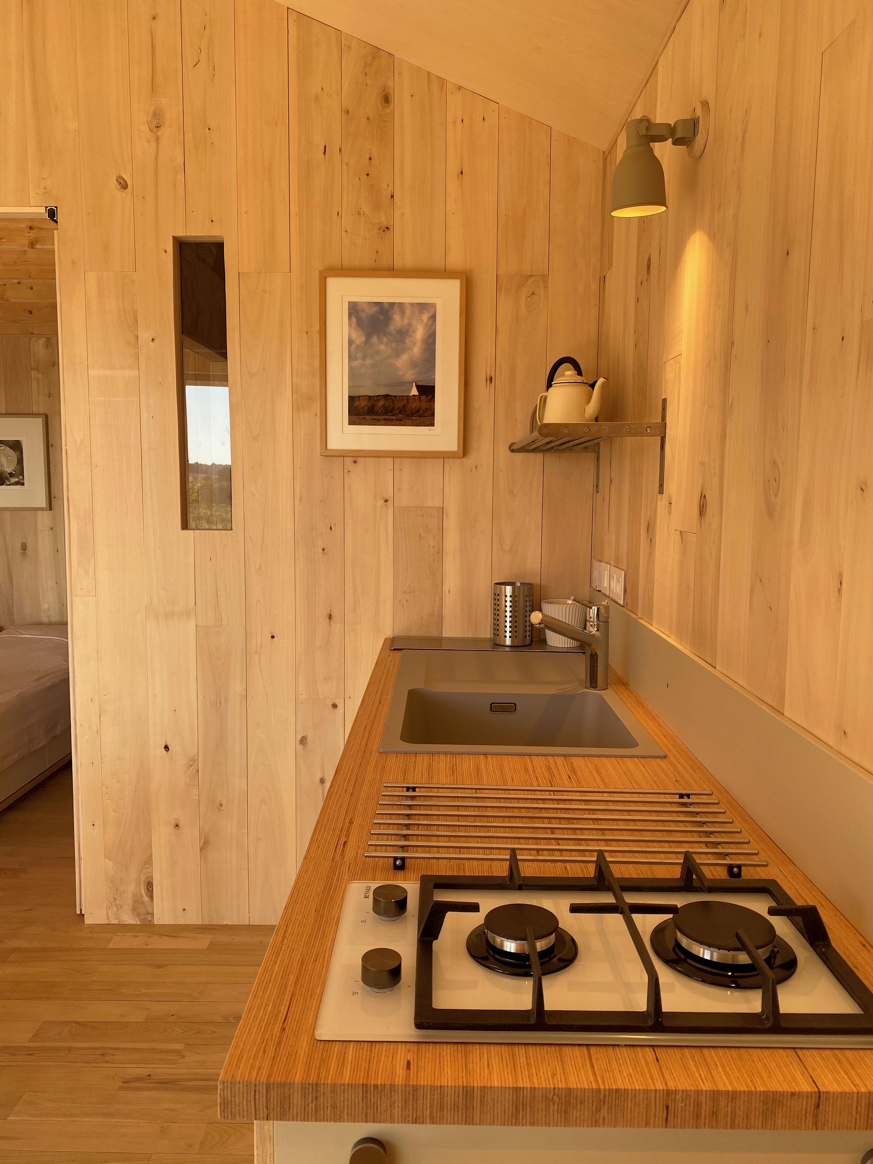 A modern kitchen with wooden walls, a gas stove, a sink, and a framed picture on the wall.