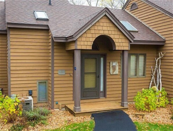Une maison à deux étages avec une entrée à l’avant, un porche couvert et un petit jardin.