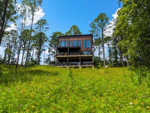 Un bâtiment moderne à deux étages, doté d’un balcon au niveau supérieur, entouré d’un champ verdoyant où poussent de nombreuses variétés de fleurs sauvages.