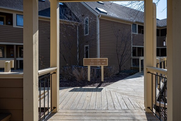 Une terrasse en bois mène à un bâtiment sur lequel est apposée une enseigne indiquant les numéros des chambres, de CI-09 à CI-15.