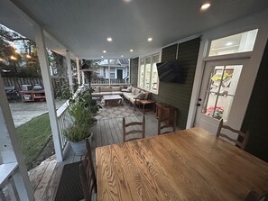 Un patio couvert comprenant une table et des chaises en bois, un canapé et un téléviseur fixé au mur.
