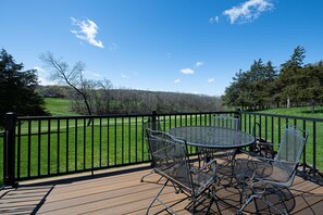 Une terrasse avec une table et des chaises donnant sur un champ verdoyant et des arbres.