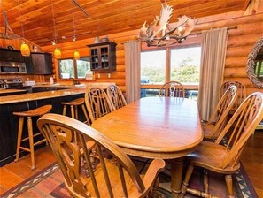 Un intérieur en bois avec une table à manger entourée de chaises, un coin cuisine avec des placards et un lustre.