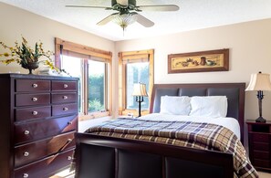 Une chambre à coucher avec un lit, une commode, des fenêtres et un ventilateur de plafond.