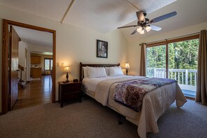 Une chambre à coucher avec un grand lit, deux tables de chevet avec des lampes, un ventilateur de plafond et une fenêtre donnant sur les arbres.