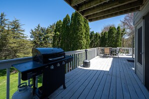 Une terrasse dotée d’un barbecue, de mobilier d’extérieur et offrant une vue sur les arbres.