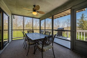 Une terrasse couverte avec une table et des chaises, de grandes fenêtres et un ventilateur de plafond.