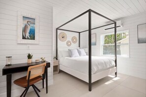 Een slaapkamer met een hemelbed, een bureau met stoel, een potplant en een klok aan de muur.