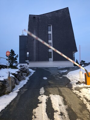 Un edificio con un diseño angular distintivo, un acceso pavimentado y suelo cubierto de nieve.