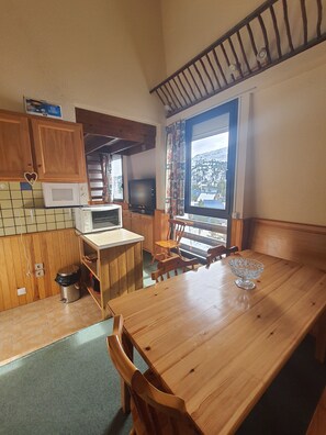 A wooden dining table with chairs, a microwave, a television, and a window with a view of a mountain. - New Listing (Arette)