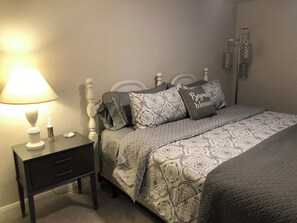 Une chambre à coucher avec un lit, une table de chevet avec une lampe et une étagère fixée au mur.