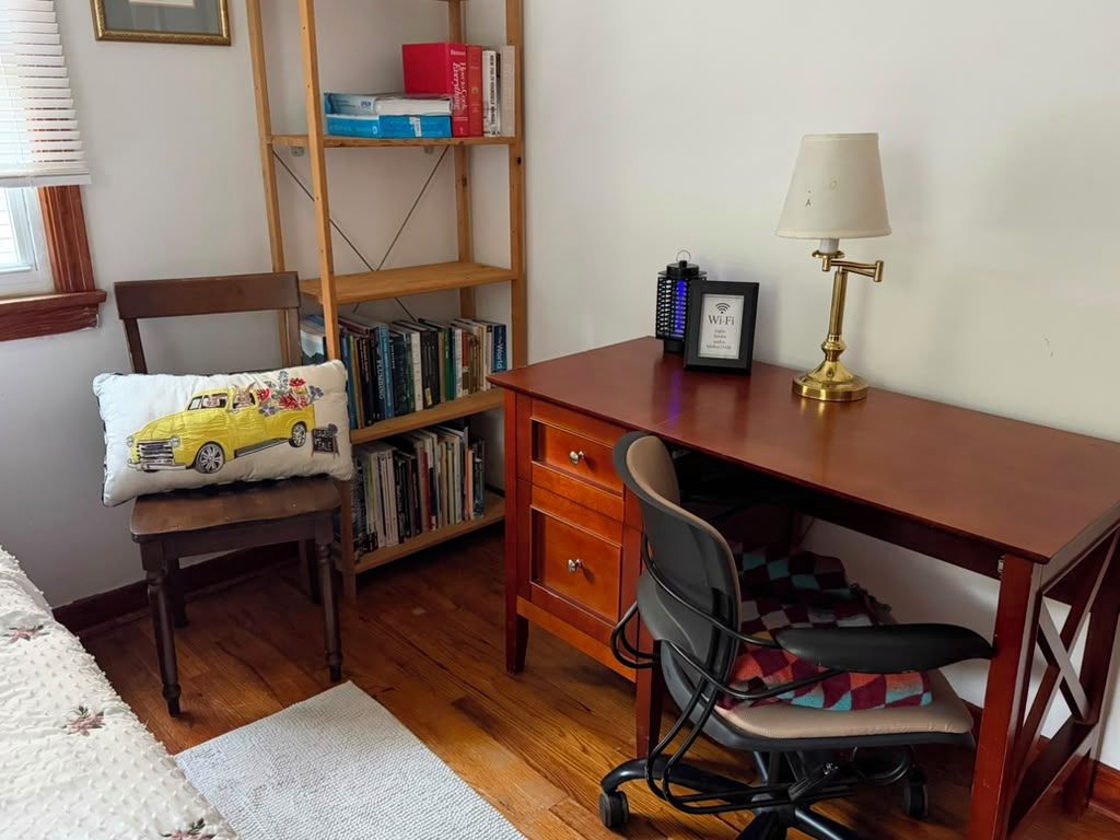 Een kamer met een houten bureau, een stoel, een boekenkast en een lamp.