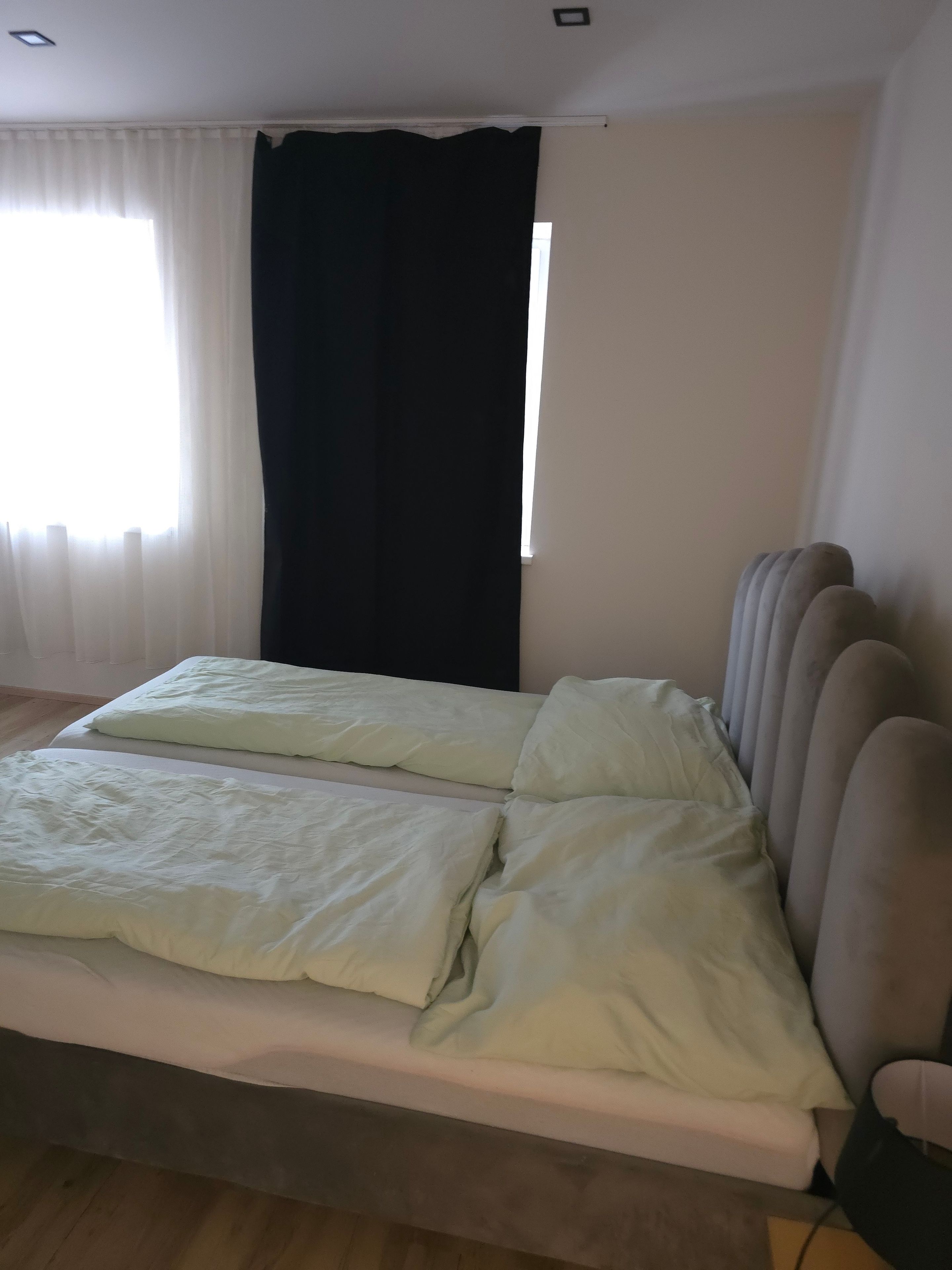 Un dormitori amb un llit, una finestra amb cortines i un radiador penjat a la paret.