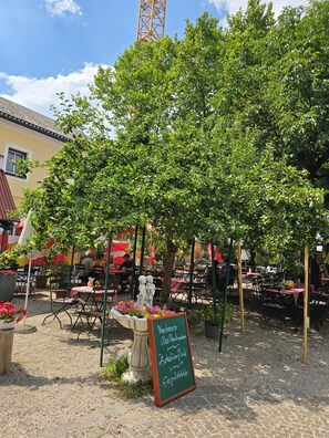 Un espace extérieur aménagé avec des tables et des chaises, entouré d’arbres et agrémenté d’un panneau noir.