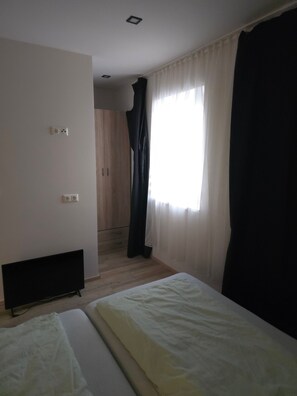 Une chambre avec un lit, une télévision, une armoire et une fenêtre avec des rideaux.