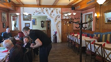 Interior de restaurant amb bigues de fusta, taules amb estovells blancs i un quadre de menús penjat a la paret.