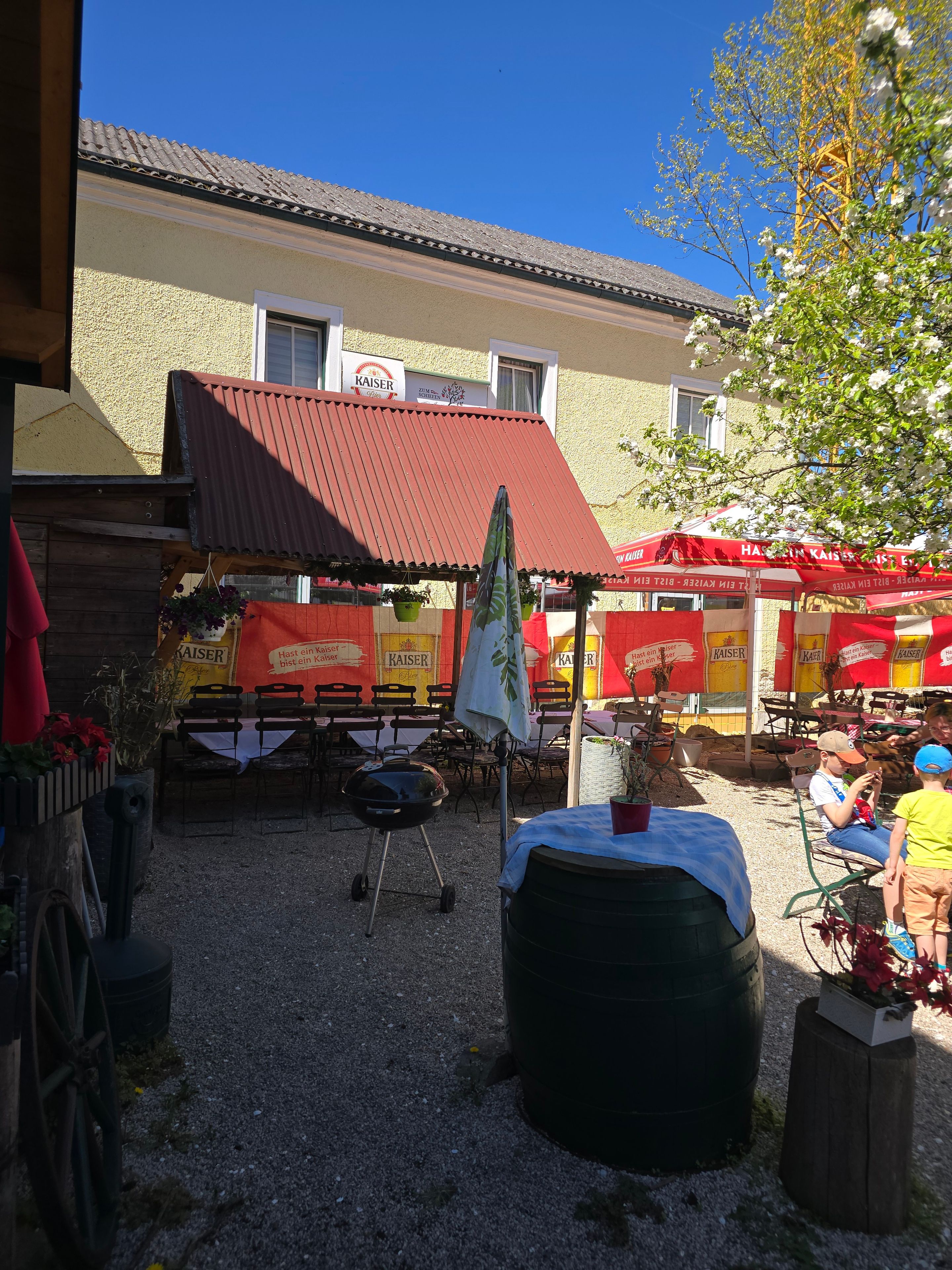 Un espace extérieur aménagé avec des tables et des chaises, un barbecue et un bâtiment avec un toit rouge en arrière-plan.