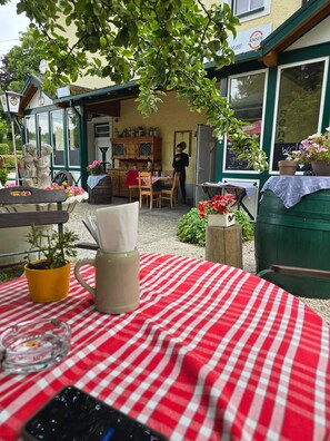 Une table recouverte d’une nappe à carreaux rouges et blancs, un pichet en verre transparent et un pot jaune contenant une plante.