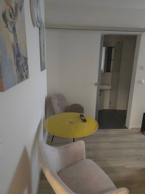 Une pièce avec une table jaune, une chaise blanche et une porte donnant sur une salle de bain.