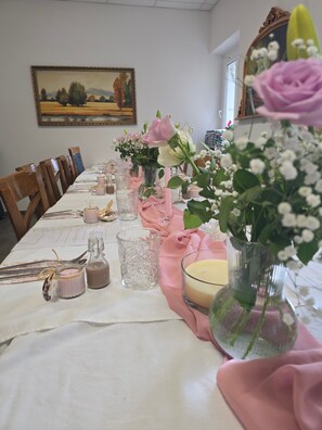 Une table à manger dressée avec des serviettes roses, de la vaisselle transparente et des centres de table floraux.