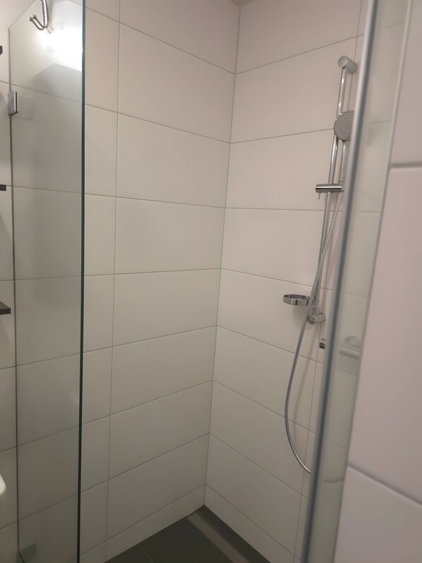 Une douche avec une porte en verre, un pommeau de douche à main et un robinet mural.