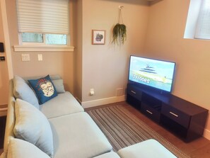 Un salon avec un canapé, un téléviseur à écran plat, une petite plante et un tableau encadré accroché au mur.
