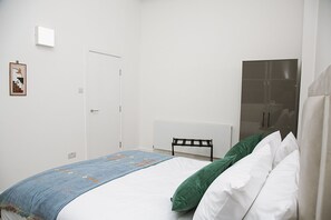 Een slaapkamer met een bed, een radiator, een deur en een ingelijste foto aan de muur.