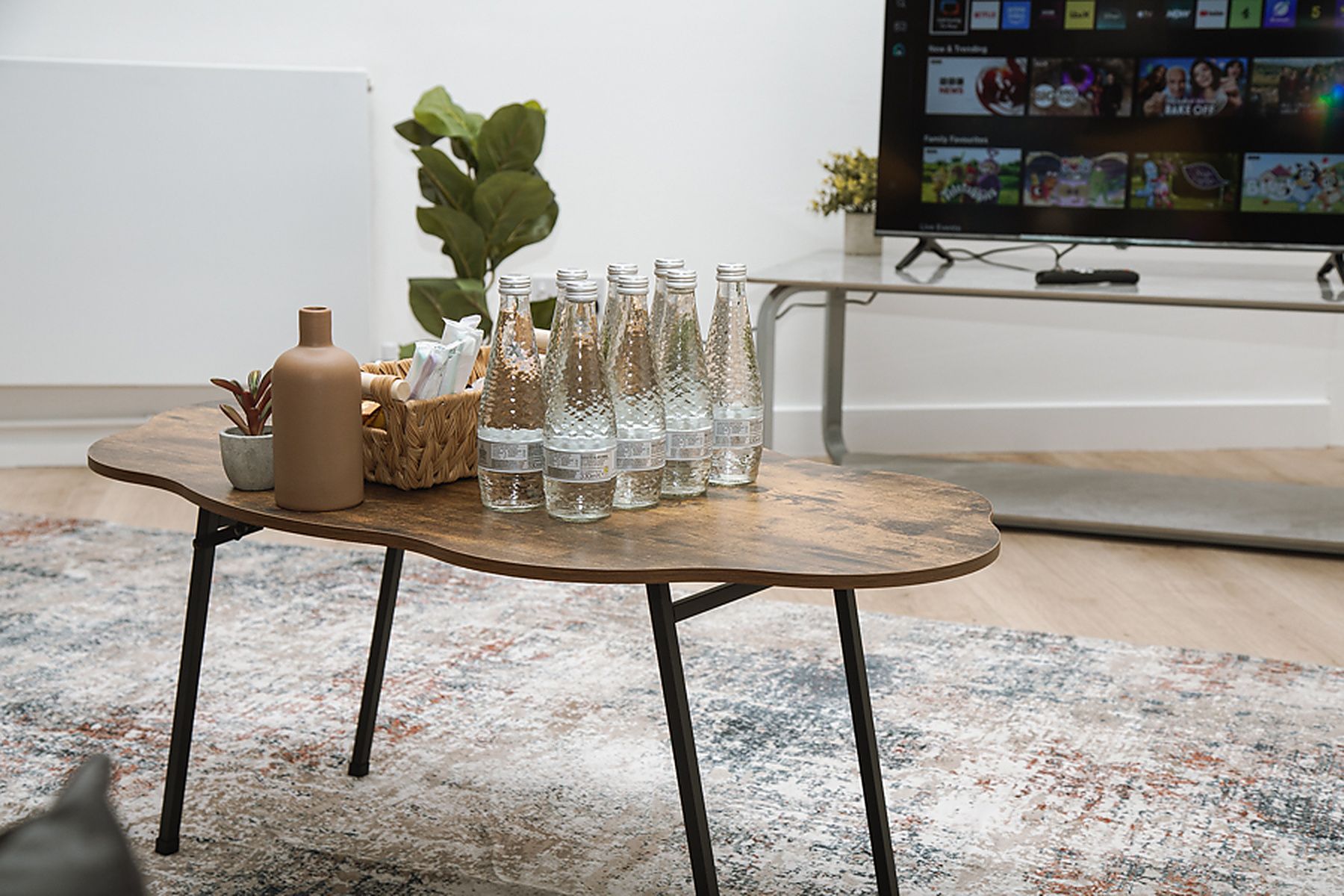 Un salon moderne avec une table basse en bois, une plante en pot et un téléviseur diffusant un film.