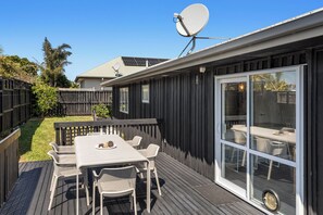 A deck with a table and chairs, a satellite dish, and a sliding glass door leading to an outdoor area. - Coastal Calm - Ohope Beach Holiday Home (Ohope)