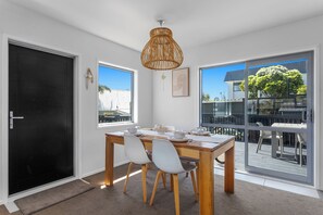A dining area with a table, chairs, and a view of the outside. - Coastal Calm - Ohope Beach Holiday Home (Ohope)