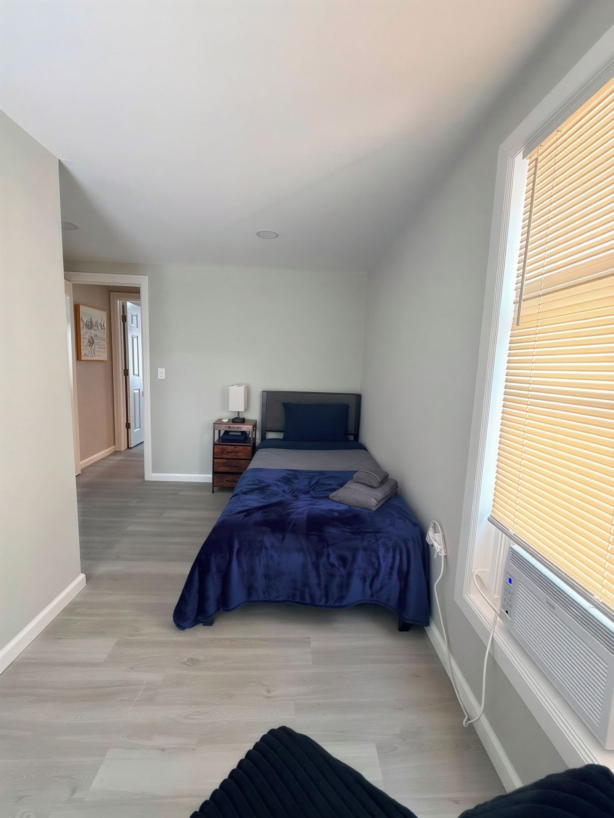 Un dormitorio con cama, mesita de noche y ventana con persianas.