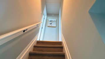 Una escalera alfombrada con barandilla, una lámpara en la parte superior y un cartel informativo enrabado en la parte inferior.