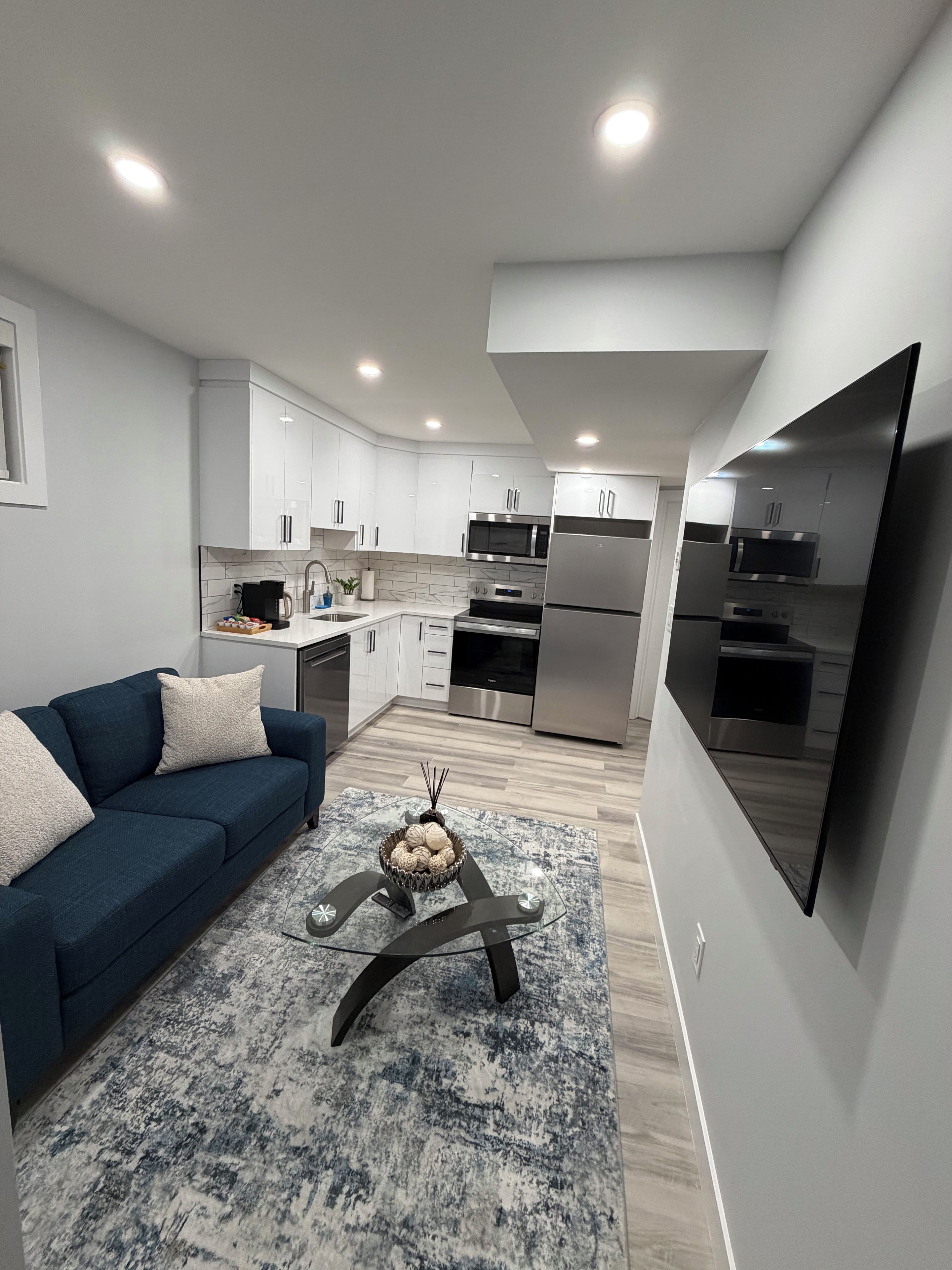 A modern kitchen with white cabinets, stainless steel appliances, and a blue sofa in the living area.