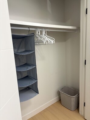 Et skab med en hvid dør, en grå kurv og en hvid bøjlestang med tøj.