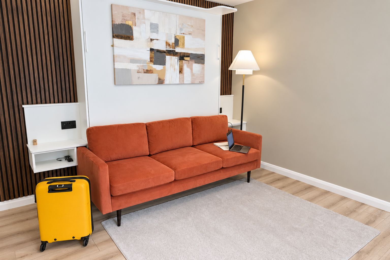 Ein Zimmer mit einer Couch, einer Lampe, einem kleinen Tisch, einem Koffer und einem Gemälde an der Wand.