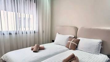 A hotel room with two beds, a ceiling-mounted air conditioner, and a window with curtains.