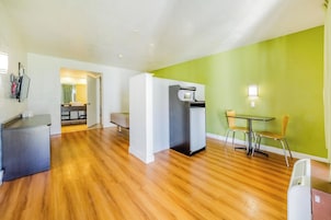 A compact living space with a kitchenette, a dining area with a table and chairs, and a bed in the background.