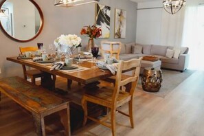 Un comedor con una mesa de madera dispuesta para cuatro personas, rodeada de sillas. Hay un sofá y un florero decorativo sobre la mesa.