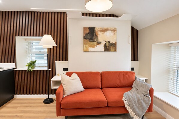 Un salon moderne avec un canapé, une lampe, un tableau et une fenêtre avec des stores.