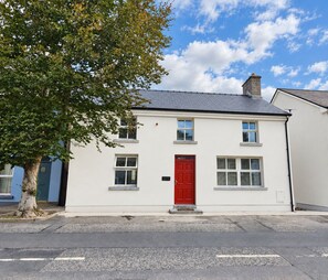 Un bâtiment à deux étages avec une porte rouge, des murs blancs et un toit gris.