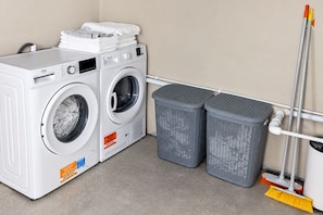 Un espace buanderie comprenant deux machines à laver, deux paniers à linge gris et un balai.